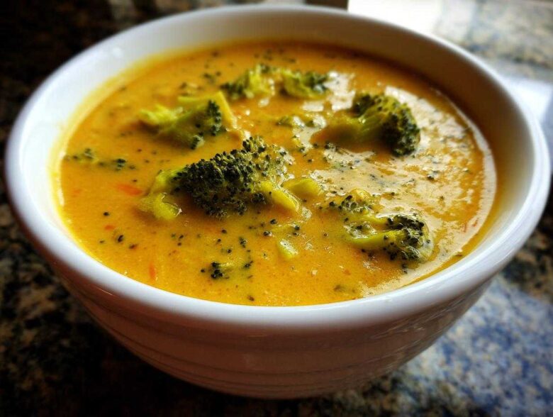 Close-up of a creamy, orange-yellow bowl of Copycat Broccoli Cheddar Soup with visible florets.