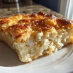 A thick, golden-brown slice of creamy Copycat Cracker Barrel Hashbrown Casserole served on a white plate.