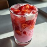 Close-up of a tall glass filled with a pink, layered Copycat Starbucks Pink Drink, topped with sliced strawberries and ice.