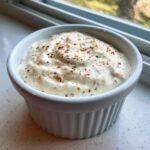A white ramekin filled with creamy Copycat Taco Bell Chicken Quesadilla Sauce, topped with visible spices.