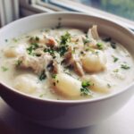 A close-up shot of a white bowl filled with rich Creamy Chicken Gnocchi Soup, topped with shredded chicken and fresh parsley.