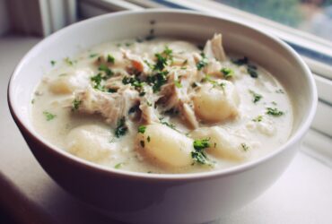 A close-up shot of a white bowl filled with rich Creamy Chicken Gnocchi Soup, topped with shredded chicken and fresh parsley.