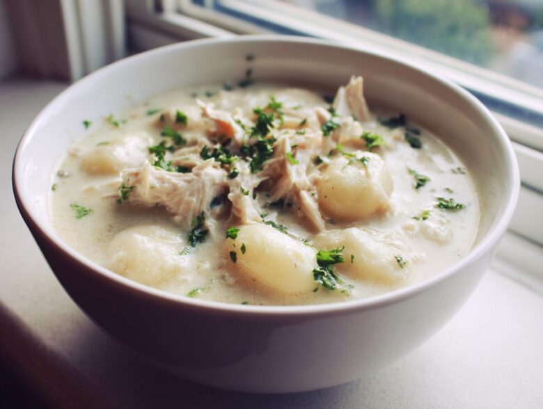 A close-up shot of a white bowl filled with rich Creamy Chicken Gnocchi Soup, topped with shredded chicken and fresh parsley.