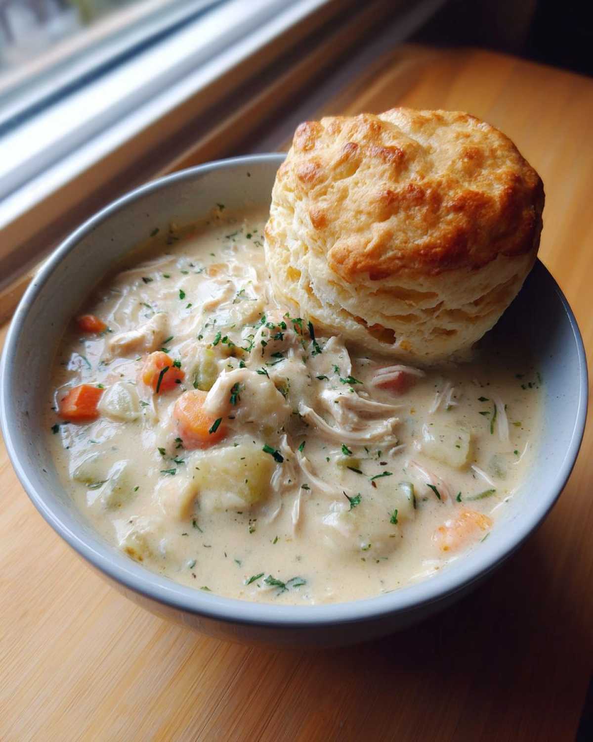 A hearty bowl of creamy Chicken Pot Pie Soup garnished with parsley, topped with a golden biscuit.