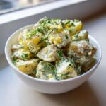 A white bowl filled with chunks of Creamy Dill Potato Salad mixed with visible pieces of hard-boiled egg and fresh dill.