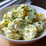 A close-up of a white bowl filled with chunks of potato coated in a creamy dressing and generously topped with fresh dill for Creamy Dill Potato Salad.