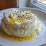 A mound of fluffy Creamy Garlic Mashed Cauliflower drizzled with melted butter and sprinkled with herbs.