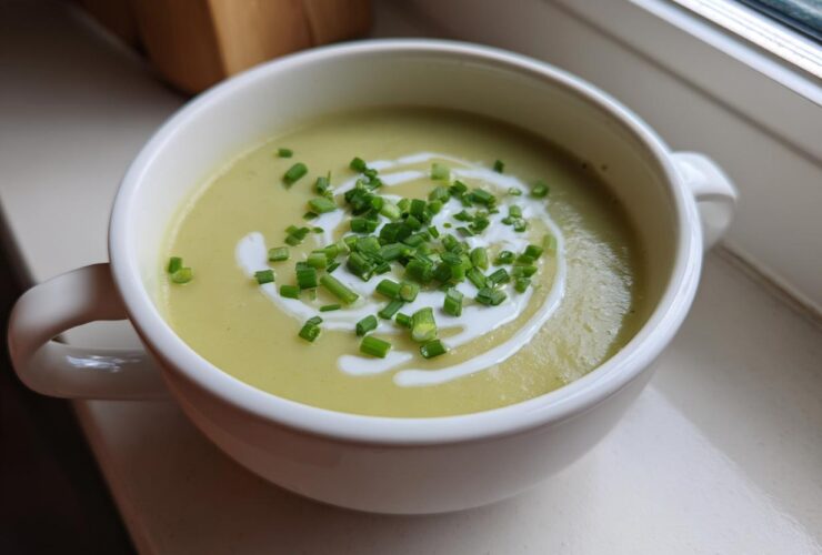 A white bowl filled with vibrant Creamy Potato Leek Soup, garnished with a swirl of cream and fresh chopped chives.