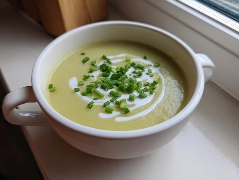 A white bowl filled with vibrant Creamy Potato Leek Soup, garnished with a swirl of cream and fresh chopped chives.