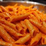 Close-up shot of penne pasta coated in a vibrant, creamy roasted red pepper pasta sauce.