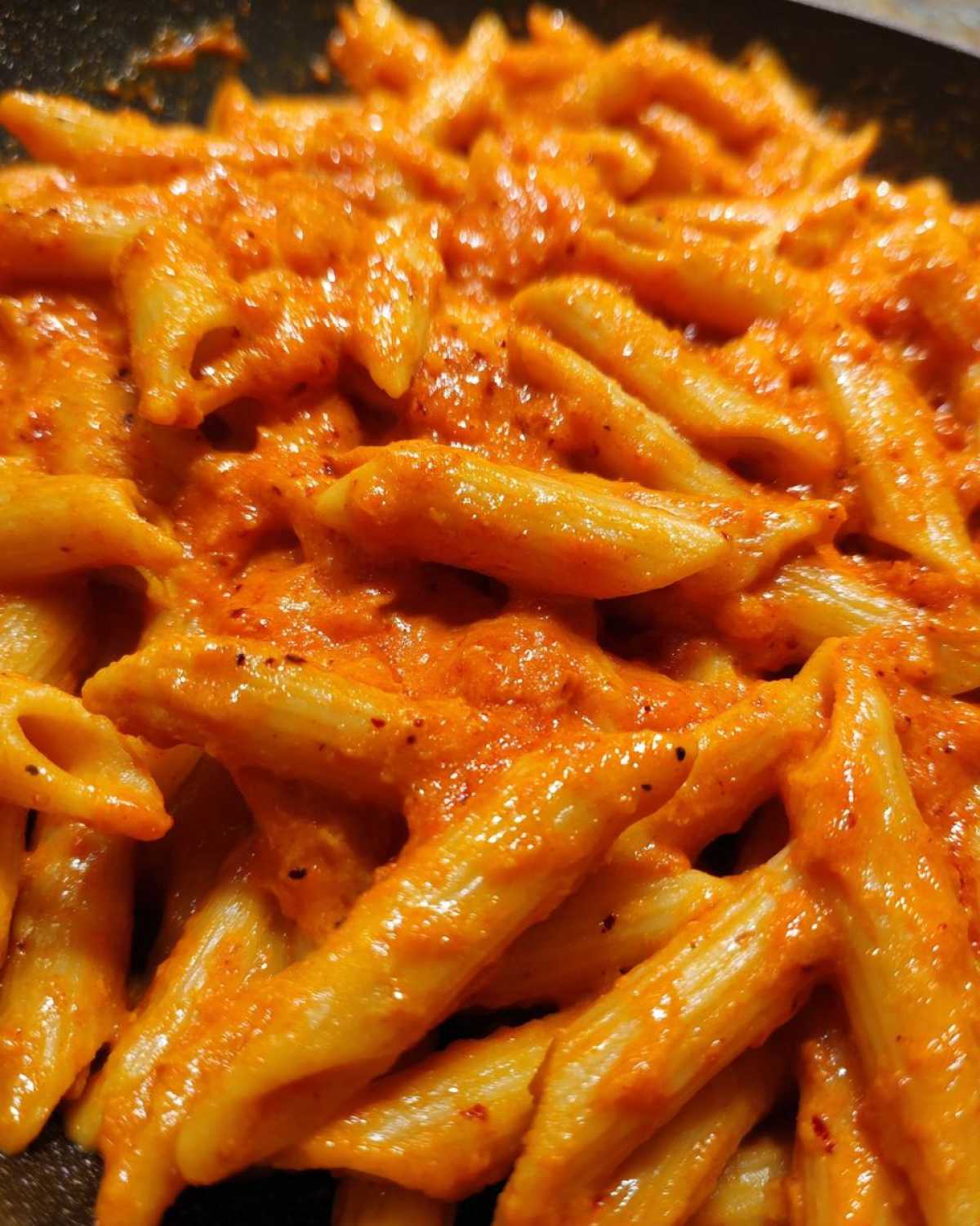 A close-up shot showing penne pasta thoroughly coated in vibrant, creamy roasted red pepper pasta sauce.
