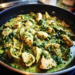Close-up of chicken pieces simmering in a rich, green sauce with spinach and artichoke hearts in a skillet.