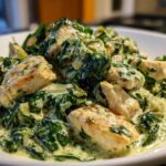 Close-up of tender chicken pieces coated in a rich, creamy sauce with spinach and artichoke hearts, ready to serve from the Creamy Spinach Artichoke Chicken Skillet.