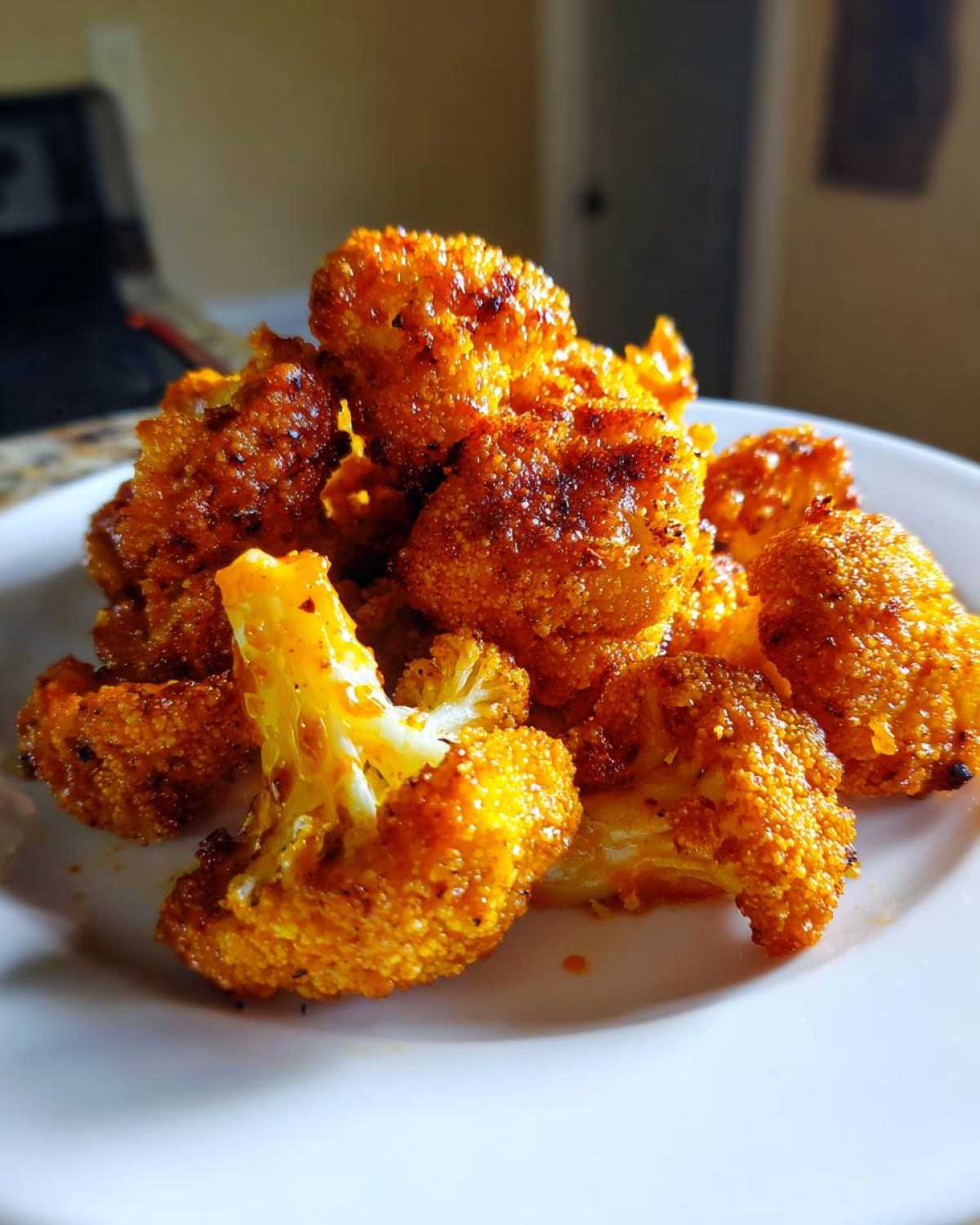 A pile of golden-brown, seasoned Crispy Air Fryer Cauliflower Wings stacked on a white plate.