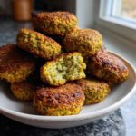 A pile of golden brown, crispy air fryer falafel in a light ceramic bowl, one broken open showing the green interior.