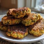 A close-up stack of golden brown, crispy air fryer falafel patties piled high on a white plate.