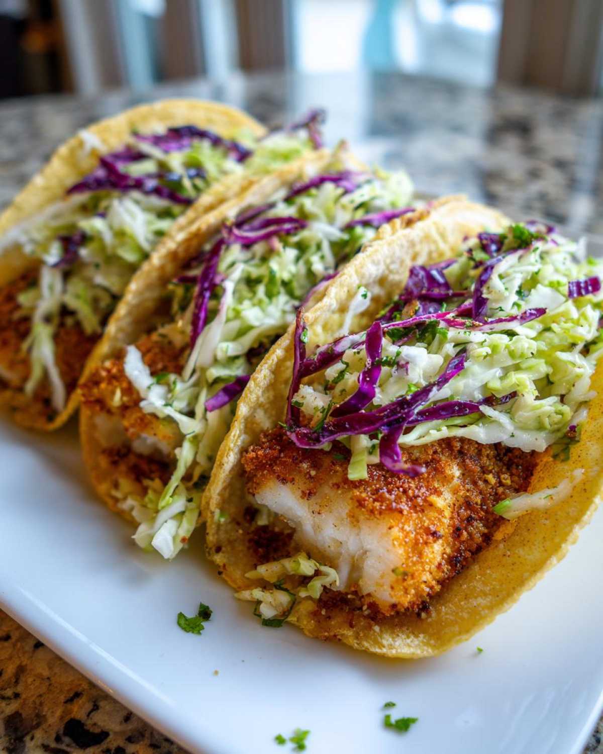 Close-up of three Crispy Baked Fish Tacos filled with white fish and topped with bright green and purple lime slaw.