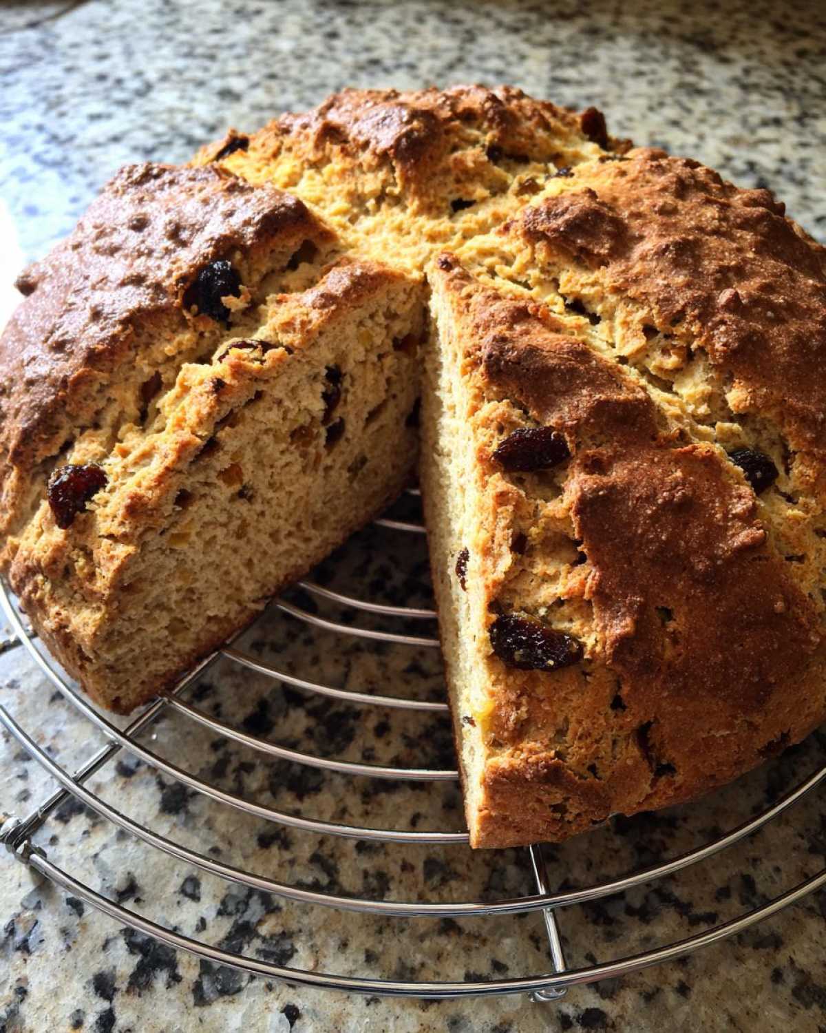 A round loaf of Easy Irish Soda Bread with Buttermilk and Raisins, cut into quarters and resting on a cooling rack.