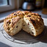 A freshly baked round of Easy Irish Soda Bread with buttermilk and raisins, cut open on a cooling rack.