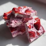 A stack of broken pieces of Frozen Strawberry Yogurt Bark topped with fresh strawberry slices.