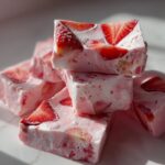 Close-up of stacked, pink Frozen Strawberry Yogurt Bark pieces with visible strawberry slices.