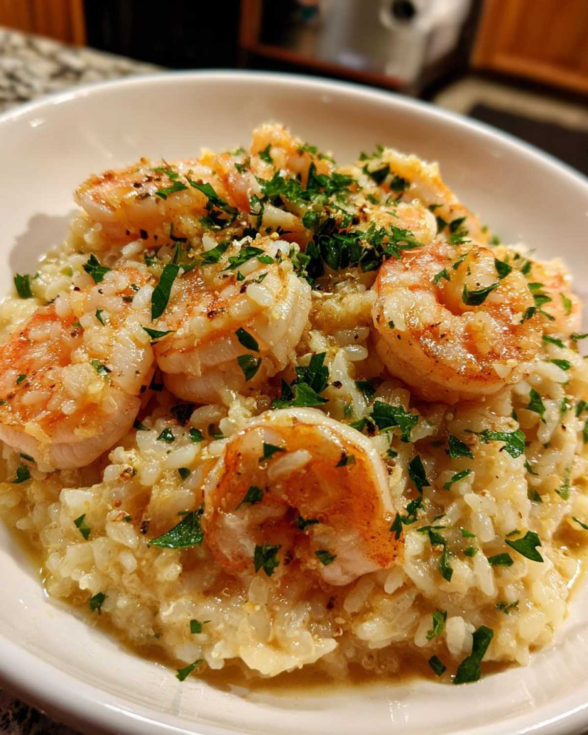 Close-up of a bowl filled with creamy rice topped with seasoned Garlic Butter Shrimp and fresh parsley.