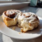 Close-up of a soft, pulled-apart Gluten-Free Cinnamon Roll topped with thick white frosting.