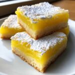 Three stacked squares of bright yellow Gluten-Free Lemon Bars with Shortbread Crust, dusted heavily with powdered sugar.