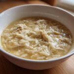 Close-up of a white bowl filled with hot Greek Lemon Chicken Soup featuring shredded chicken and orzo pasta.
