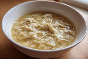 Close-up of a white bowl filled with hot Greek Lemon Chicken Soup featuring shredded chicken and orzo pasta.