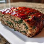 A thick slice of Healthy Turkey Spinach Meatloaf topped with a bright red glaze, showing green spinach mixed throughout the meat.