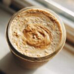 Overhead close-up of High-Protein Peanut Butter Overnight Oats topped with a swirl of peanut butter in a glass jar.