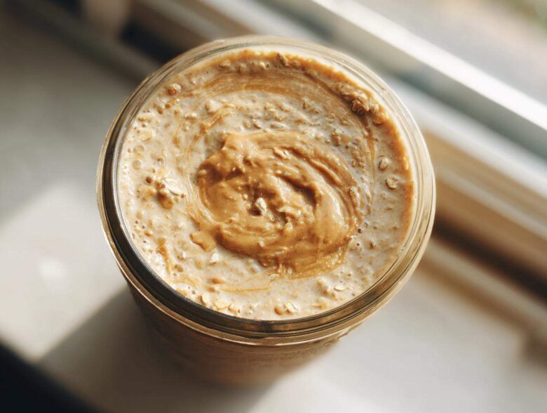 Overhead close-up of High-Protein Peanut Butter Overnight Oats topped with a swirl of peanut butter in a glass jar.
