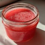 Close-up of bright red Homemade Strawberry Lemonade Concentrate filling a small glass jar.