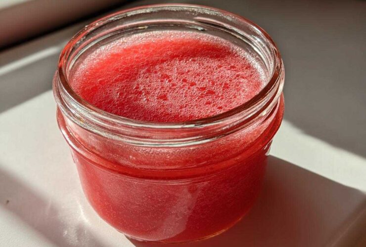 Close-up of bright red Homemade Strawberry Lemonade Concentrate filling a small glass jar.