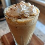 Close-up of a tall glass filled with a blended Homemade Vanilla Bean Frappuccino, topped with whipped cream and a dusting of spice.