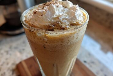 Close-up of a tall glass filled with a blended Homemade Vanilla Bean Frappuccino, topped with whipped cream and a dusting of spice.