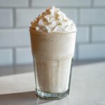 A tall glass of Homemade Vanilla Bean Frappuccino topped high with whipped cream and a dusting of spice.