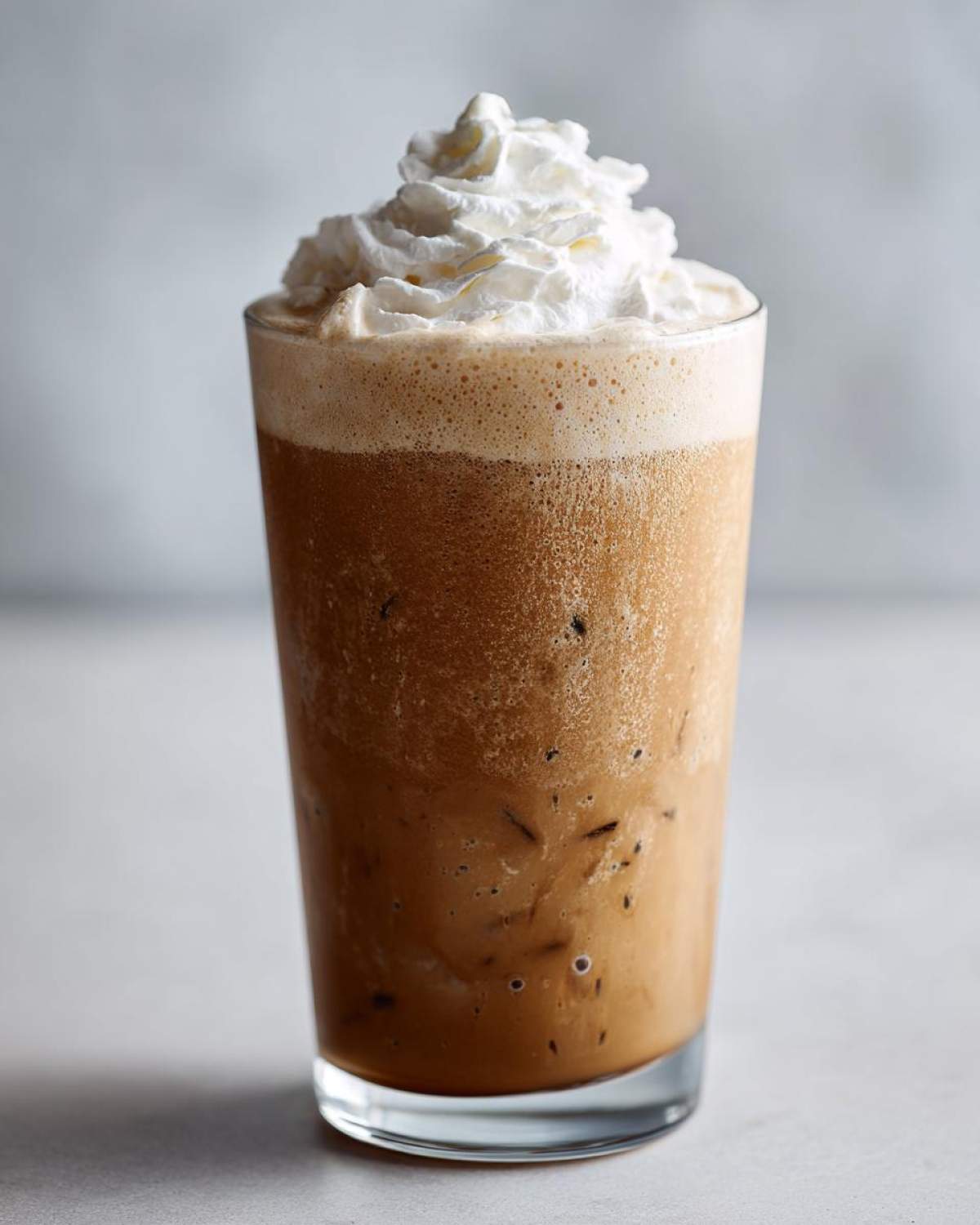 A tall glass filled with a blended Homemade Vanilla Bean Frappuccino topped high with whipped cream.