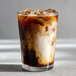 Close-up of an Iced Brown Sugar Oatmilk Latte with rich coffee swirling into white oatmilk over ice cubes.