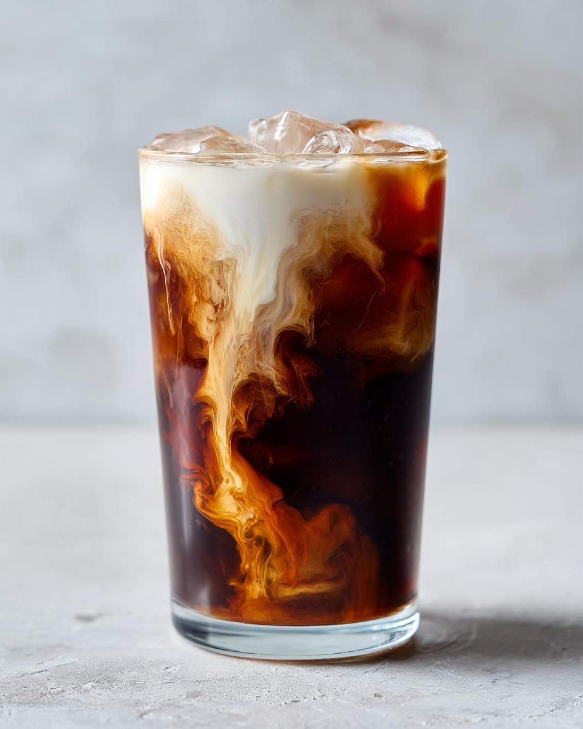 Close-up of an Iced Brown Sugar Oatmilk Latte showing the creamy oatmilk swirling into the dark coffee and ice.