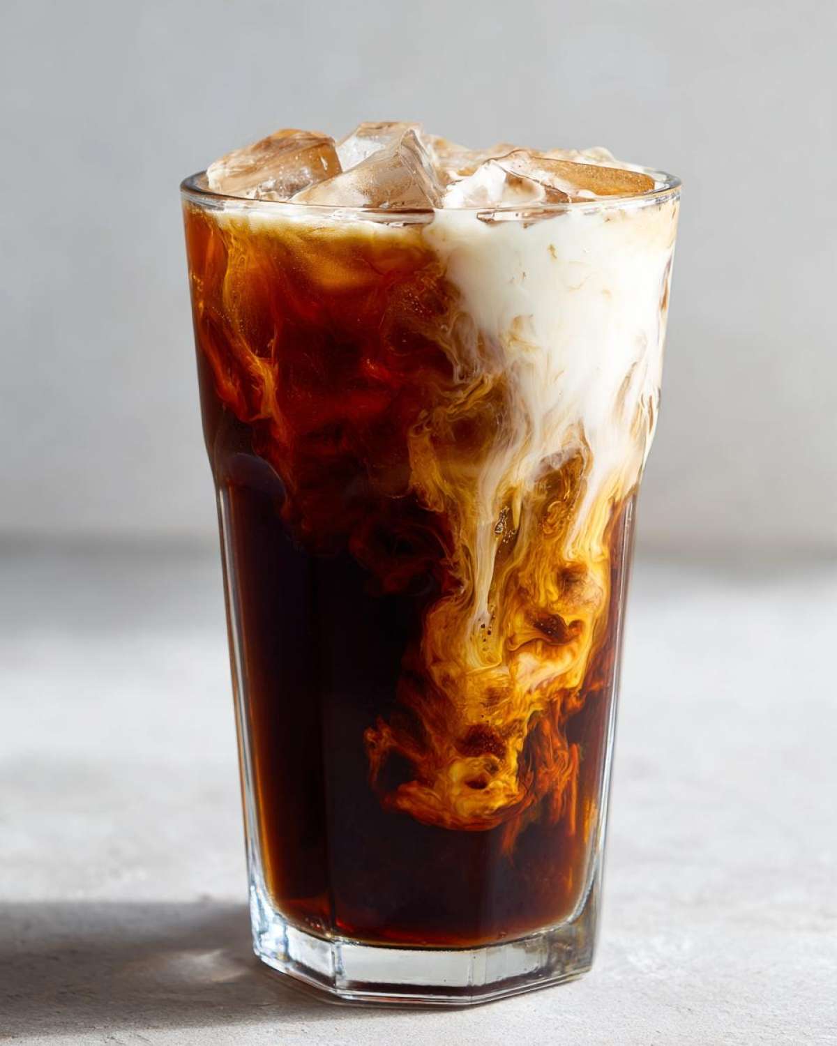 Close-up of an Iced Brown Sugar Oatmilk Latte showing oatmilk swirling beautifully into dark espresso.