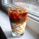 A tall glass filled with a layered Iced Caramel Macchiato, showing milk, caramel drizzle, and espresso over ice.