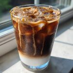 A tall glass of Iced Caramel Macchiato showing distinct layers of milk, espresso, and caramel drizzle over ice.