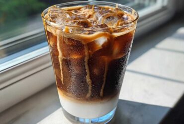 A tall glass of Iced Caramel Macchiato showing distinct layers of milk, espresso, and caramel drizzle over ice.