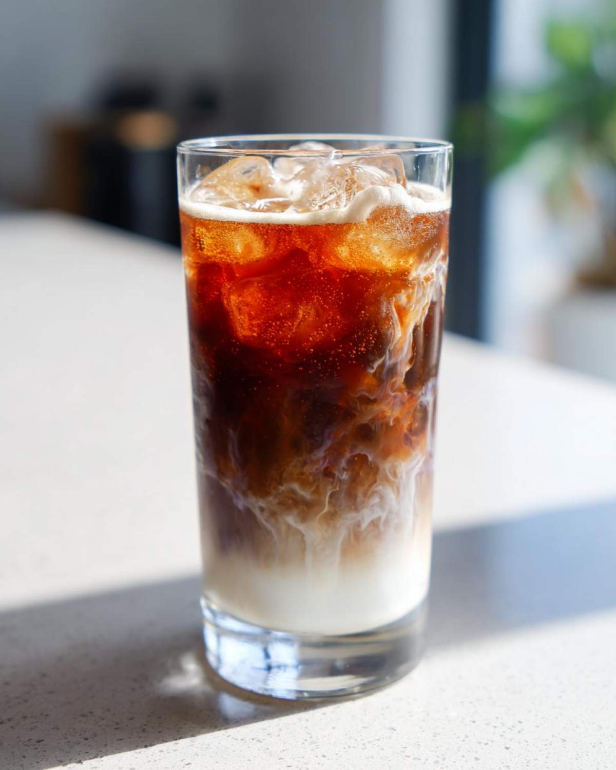 Close-up of an Iced Lavender Latte showing rich coffee mixing with white milk and ice cubes in a tall glass.
