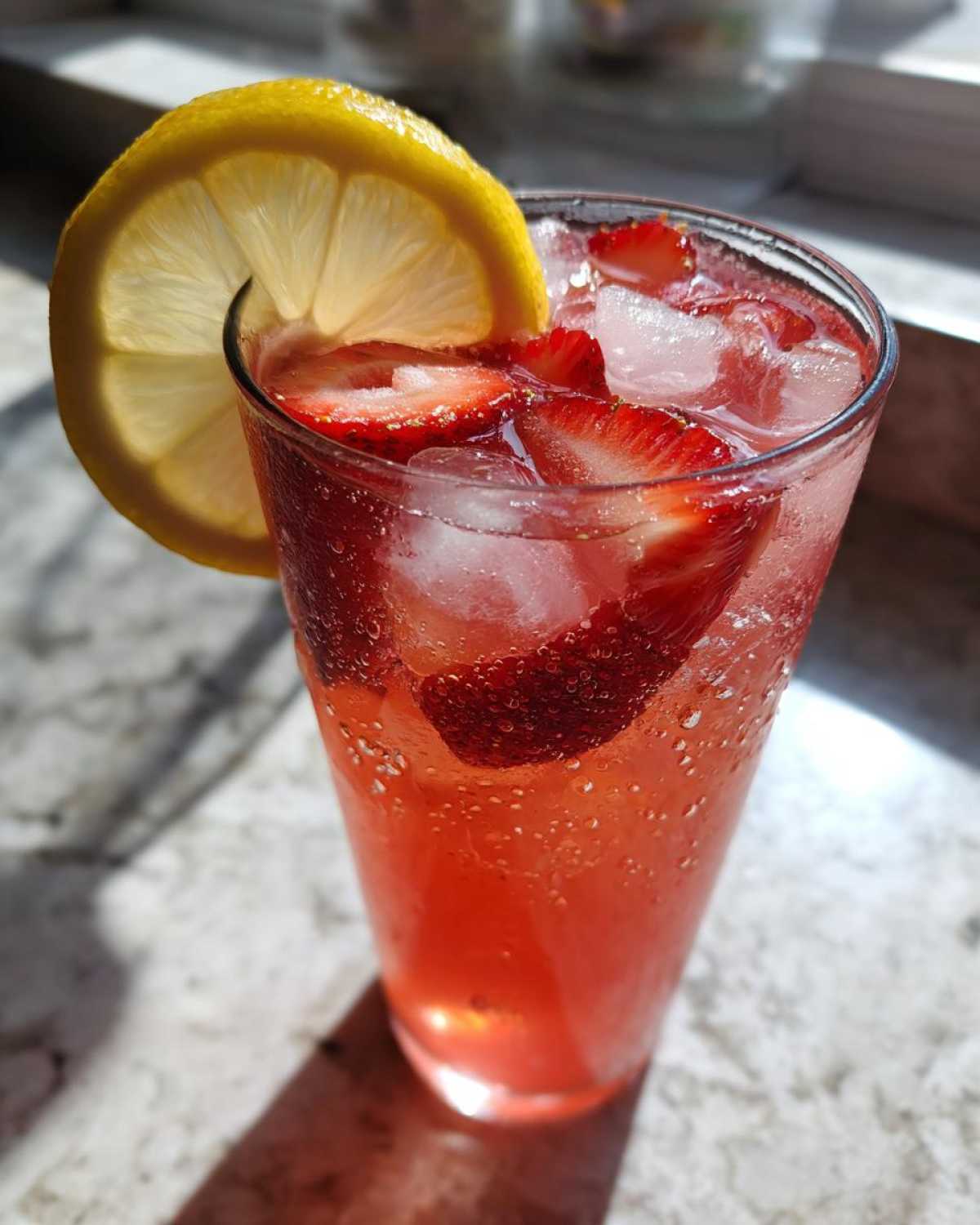 Close-up of a tall glass filled with Iced Strawberry Lemon Tea, ice, sliced strawberries, and a lemon wheel garnish.