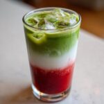 Close-up of a vibrant Iced Strawberry Matcha Latte showing distinct red, white, and green layers over ice.