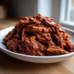 Close-up of richly sauced, shredded Instant Pot Beef Barbacoa piled high in a white serving bowl.
