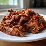 A close-up of shredded, saucy Instant Pot Beef Barbacoa piled high on a white plate.